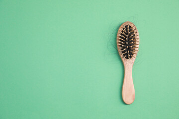 Wooden brush with lost hair on green background, top view. Space for text
