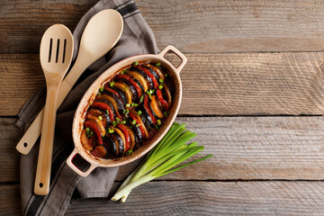 Delicious ratatouille, green onions, spoon and spatula on wooden table, flat lay. Space for text