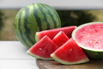 Delicious cut and whole ripe watermelons on white wooden table outdoors, closeup