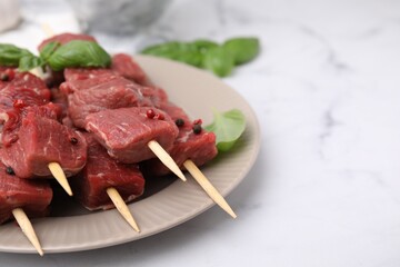 Wooden skewers with cut fresh beef meat, basil leaves and spices on white table, closeup. Space for text