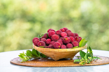 Arbutus berries or Red Yangmei in basket over green natural Blur background, Red Yangmei fruit in wooden basket over blur greenery background.