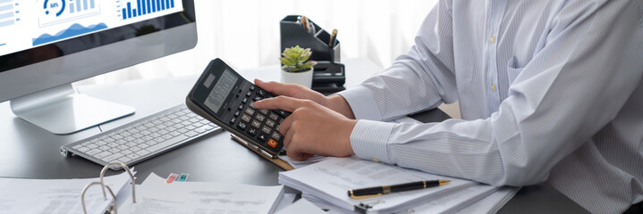 Corporate auditor calculating budget with calculator on his office desk. Dedicated accountant...
