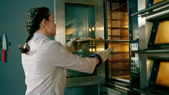 attractive baker takes ready buns and croissants from professional oven bakery production fresh baked goods