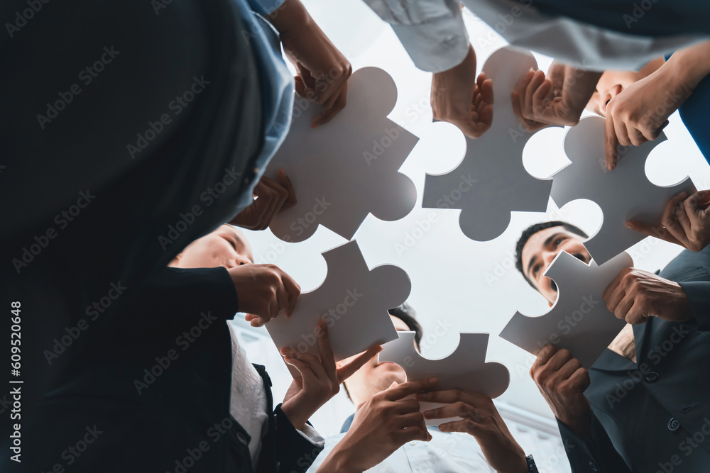Poster below view of diverse corporate officer workers collaborate in office connecting puzzle pieces as pa