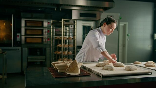 concentrated beautiful woman baker forms raw bread buns before baking bakery production of pastries