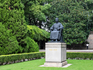 Bronze statue of Lu Xun sitting on chair at Lu Xun Park, Hongkou District, Shanghai, China.  Famous Chinese writer, essayist, poet and literary critic. - obrazy, fototapety, plakaty