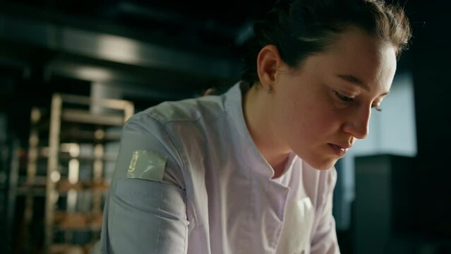 beautiful woman baker cuts patterns with a professional baker's knife on raw bread buns before baking bakery production of pastries