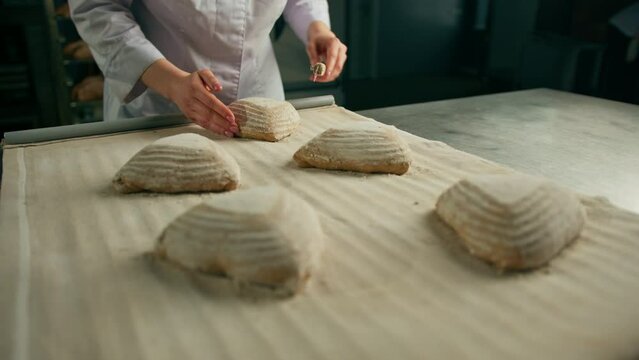 woman baker cuts patterns on raw bread rolls with a professional baker's knife before baking bakery production of pastries close-up