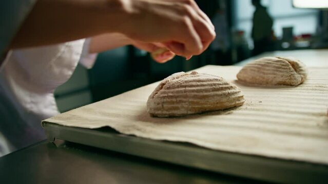 woman baker cuts patterns on raw bread rolls with a professional baker's knife before baking bakery production of pastries close-up