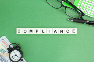 a calculator, glasses, banknotes and an alarm clock with the word compliance. compliance concept