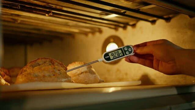 baker measures the temperature of freshly baked bread in the oven with a thermometer bakery production of pastries