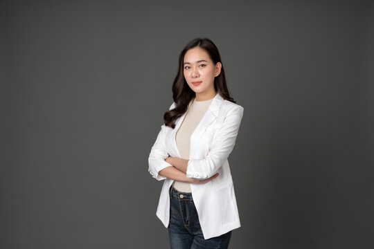 An Asian female executive with long hair stood with her arms crossed, confident and determined. She wore a white suit. and stand to take pictures with a gray scene in the studio
