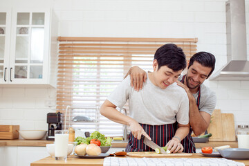 Happy cheerful LGBTQ+ gay romantic couple preparing and making a sandwich together in the kitchen. Diversity in ethnicity, nationality, and sex concept. LGBTQ+ married people lifestyles.