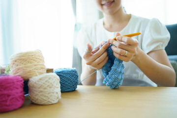 Happy cheerful Asian woman doing a crochet in living room in free time. 