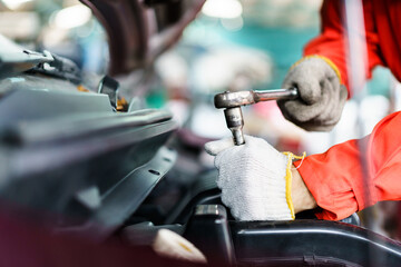 Automobile technician working in auto garage, technician holding a wrench preparing to repair broken vehicle. Professional auto or car repairman fixing a crashed car.