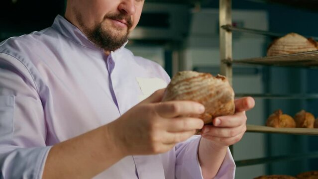 Male baker holding and smelling and checking freshly baked fragrant bread in bakery industry