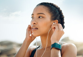 Woman with earphones, fitness at the beach and listening to music for motivation and workout outdoor. Exercise, health and wellness, female athlete streaming online with radio and audio in nature