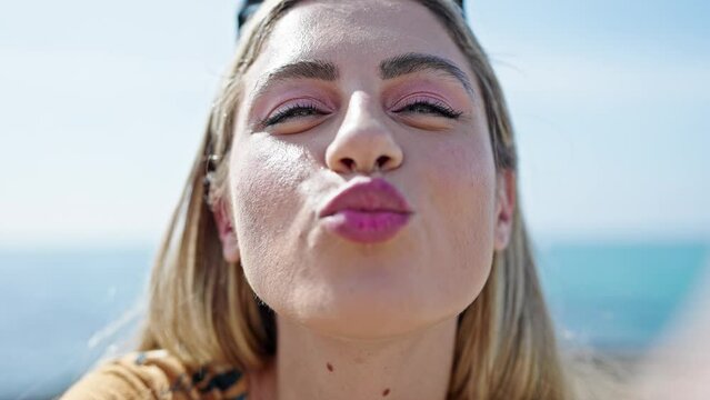 Young blonde woman making selfie by the smartphone kissing at seaside