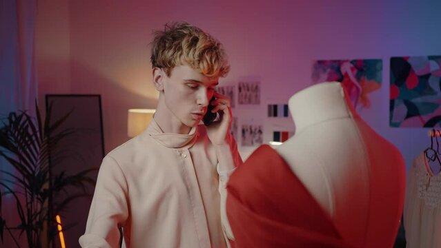 Slow motion non-binary tailor discussing new collection on mobile phone in clothing design studio