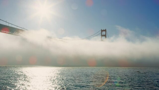 Thick fog surrounds Golden Gate Bridge silhouetted by bright sun