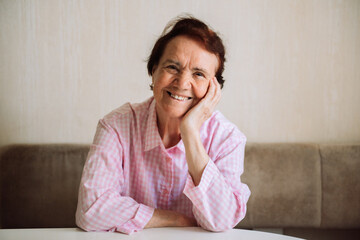 Portrait of happy senior lady sitting at home, closeup, copy space. Attractive old woman with short hair smiling at camera