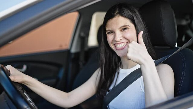 Young beautiful hispanic woman sitting on car doing thumb up gesture at street
