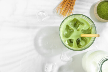 Iced green matcha latte in a glass on white background with hard shadows. Cold summer drink. Top...