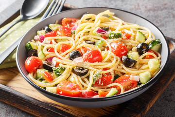 Spaghetti pasta with olives, tomatoes, onions, cucumbers and bell pepper close-up in a bowl on the table. horizontal