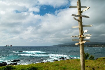 Wooden Post with Direction Signs at Hanga Roa Waterfront.  Easter Island Chile Pacific Ocean Coastline, Stormy Skyline with Distant Cargo Ship on Horizon