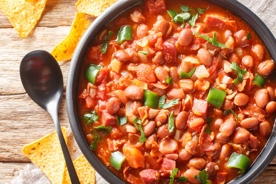 Frijoles charros is a traditional Mexican dish made of pinto beans stewed with onion, garlic, and bacon closeup on the bowl on the table. Horizontal top view from above