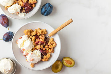 Plum crumble with vanilla ice cream on white background. Summer crispy fruit dessert. Top view with...
