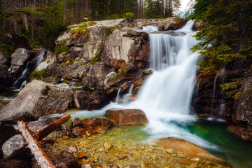 Stunning scenery of the rapids of a Dlhy waterfall flowing through rocky mountains in a green forest. National Park High Tatra, Slovakia,