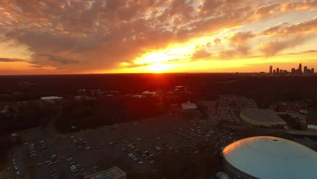 Aerial Panning Shot Of Vehicles In Parking Lots By Bojangles Coliseum, Drone Flying Over City Against Orange Cloudy Sky At Sunset - Charlotte, North Carolina