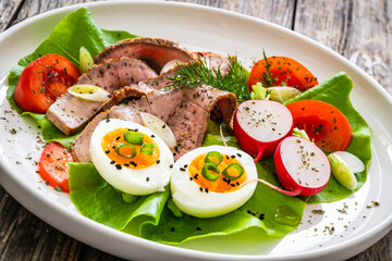Tasty salad - roasted beef loin boiled eggs and fresh vegetables on wooden table
