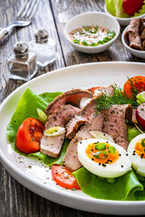 Tasty salad - roasted beef loin boiled eggs and fresh vegetables on wooden table
