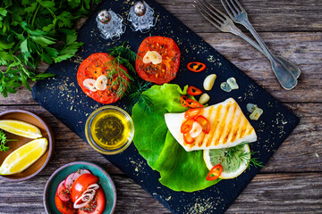 Grilled calamari steak with fried tomatoes and fresh vegetables on wooden table
