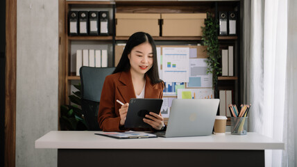 Asian young businesswoman working in the office with working notepad, tablet and laptop documents