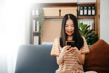 Asian woman using the smartphone and tablet on the sofa at home.