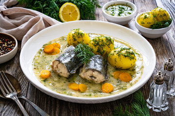 Cooked eel steaks and boiled tomatoes in dill sauce served on wooden table
