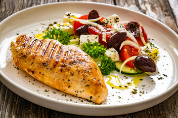 Seared chicken breast and Greek salad on wooden table
