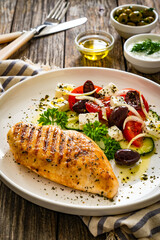 Seared chicken breast and Greek salad on wooden table
