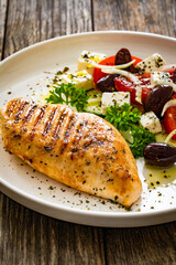 Seared chicken breast and Greek salad on wooden table
