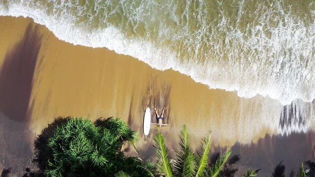 4K drone shooting from above showing man prostrated on beach after intense surfing session. Surfing, active lifestyle, spending time at beach, exotic warm countries concept.