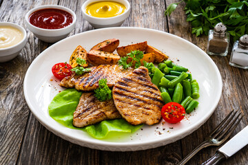 Grilled pork loin steaks with green beans and fried potatoes on wooden table
