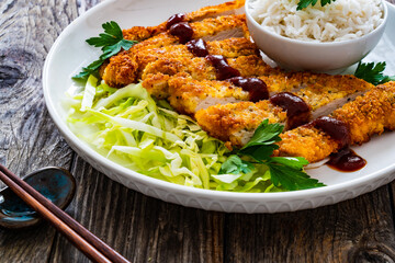 Tonkatsu - crispy Japanese pork chop with white rice and  fresh vegetables on wooden table