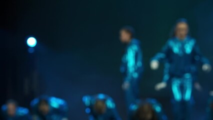 A group of dancers in colorful costumes dance on stage. Blurred background. Dance show concert. Choreography and rhythm in dance. Creative dance.