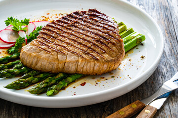 Grilled beef steak with green asparagus on wooden table

