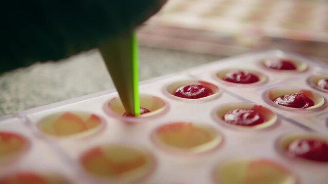 Pastry chef makes chocolates Tempering chocolate pours melted chocolate from a pastry sleeve into a mold professional kitchen
