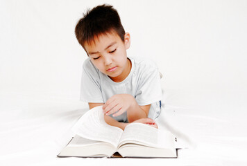 A thinking or daydreaming boy doing homework with glasses, a notebook and a pencil, reading a book highlighted on a white background
