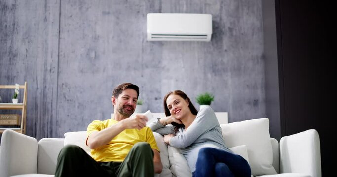 Happy Young Couple Adjusting Temperature Of Air Conditioner